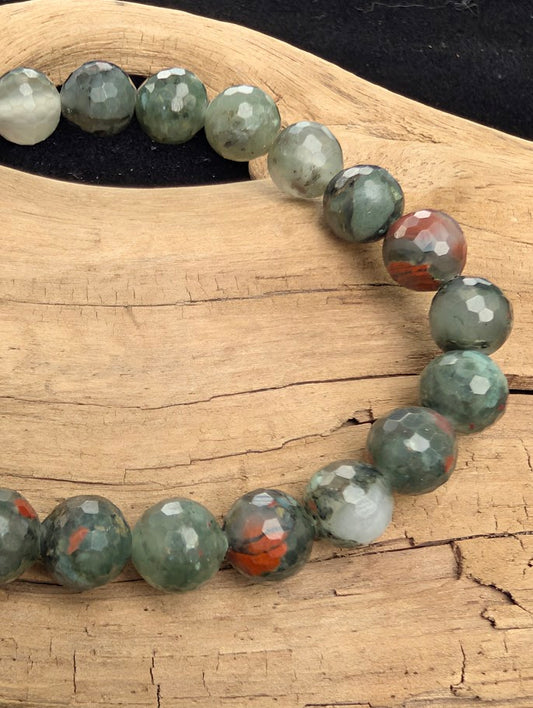 Macro close-up of 8mm faceted African Bloodstone beads highlighting the geometric cut and the natural red hematite spots within the green chalcedony matrix.