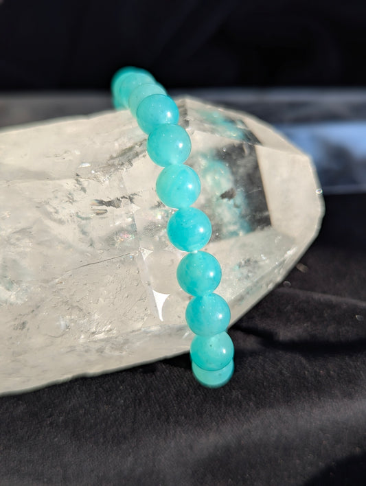 Macro view of an 8mm premium Amazonite beaded bracelet on a static background, highlighting the vitreous surface finish and subtle silken perthitic chatoyancy across the microcline feldspar spheres.