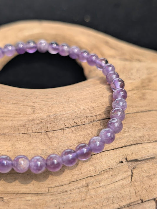Macro view of polished 4mm Amethyst spherical beads on driftwood, highlighting natural internal quartz veils and color zoning.