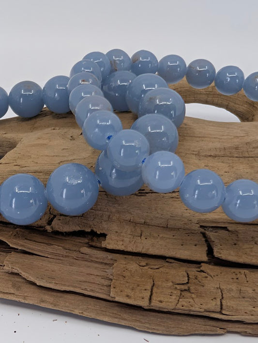 Close-up of high quality Angelite beads on wood highlighting smooth polish and consistent blue colour