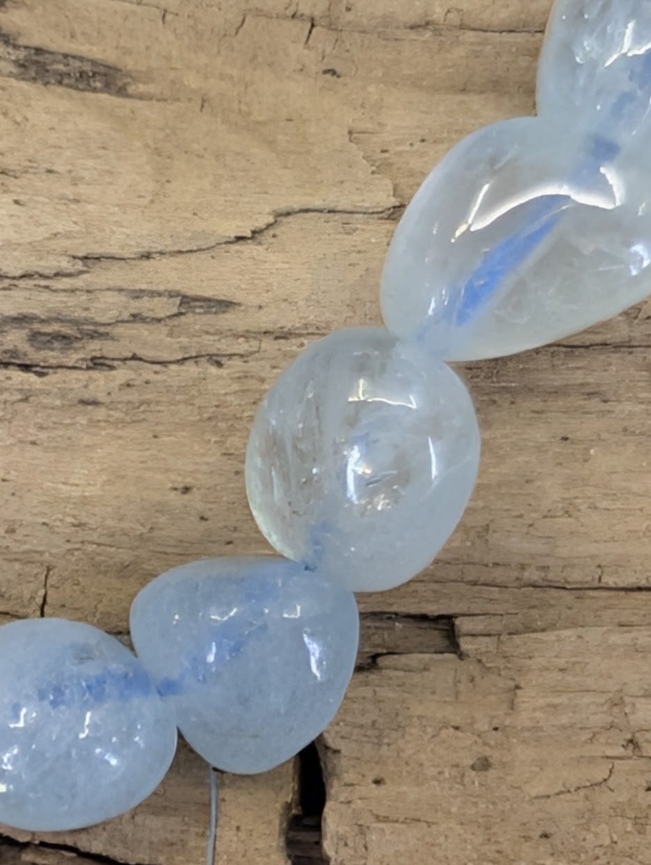 A collection of natural freeform Aquamarine nugget bead bracelets, displayed on a natural wood surface to highlight the organic shape and icy-blue color variation.