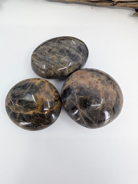 Three polished Black Moonstone palm stones showing dark feldspar banding and sheen
