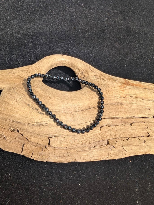 3mm faceted Black Tourmaline beaded stretch bracelet resting on a driftwood display, showing reflective cuts.