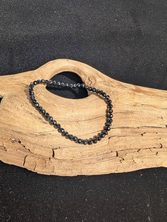 3mm faceted Black Tourmaline beaded stretch bracelet resting on a driftwood display, showing reflective cuts.