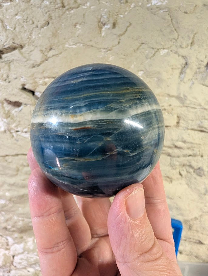 Side view of banded calcite sphere with ocean blue tones and white stripe