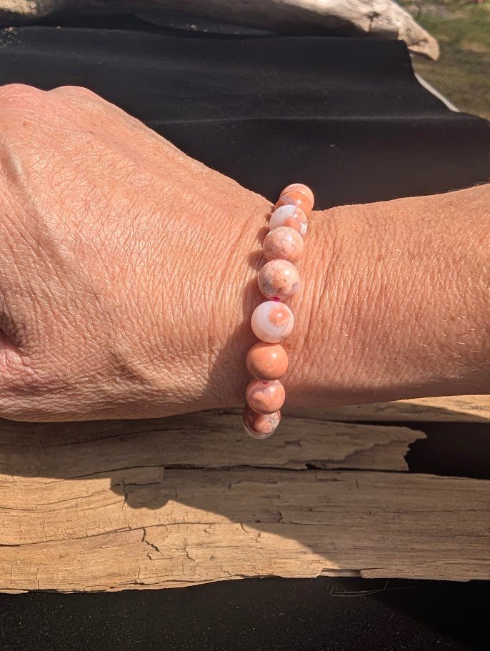 Natural sunlight on an intricately banded 8mm pink Cotton Candy Agate stretch bracelet worn on a wrist.