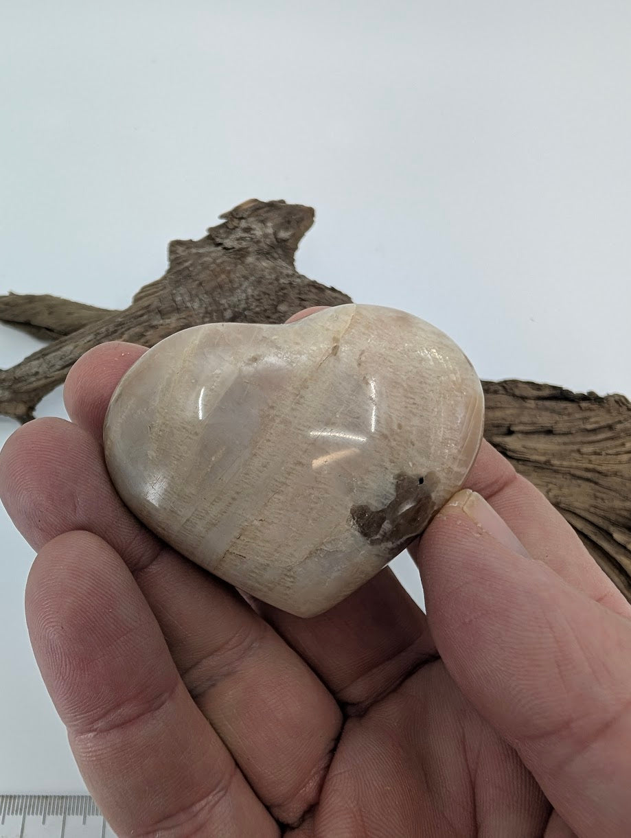 Hand holding a 90g Cream Moonstone heart showing silky luster.