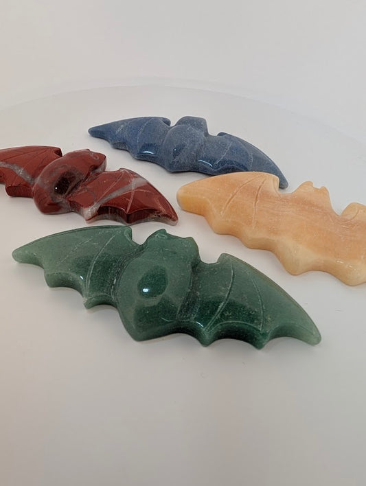 Angled view of red jasper, green aventurine, blue aventurine, and yellow calcite bat carvings