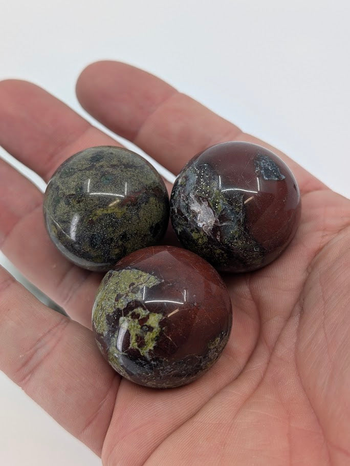 Three Dragon Blood Stone mini spheres in hand for size reference