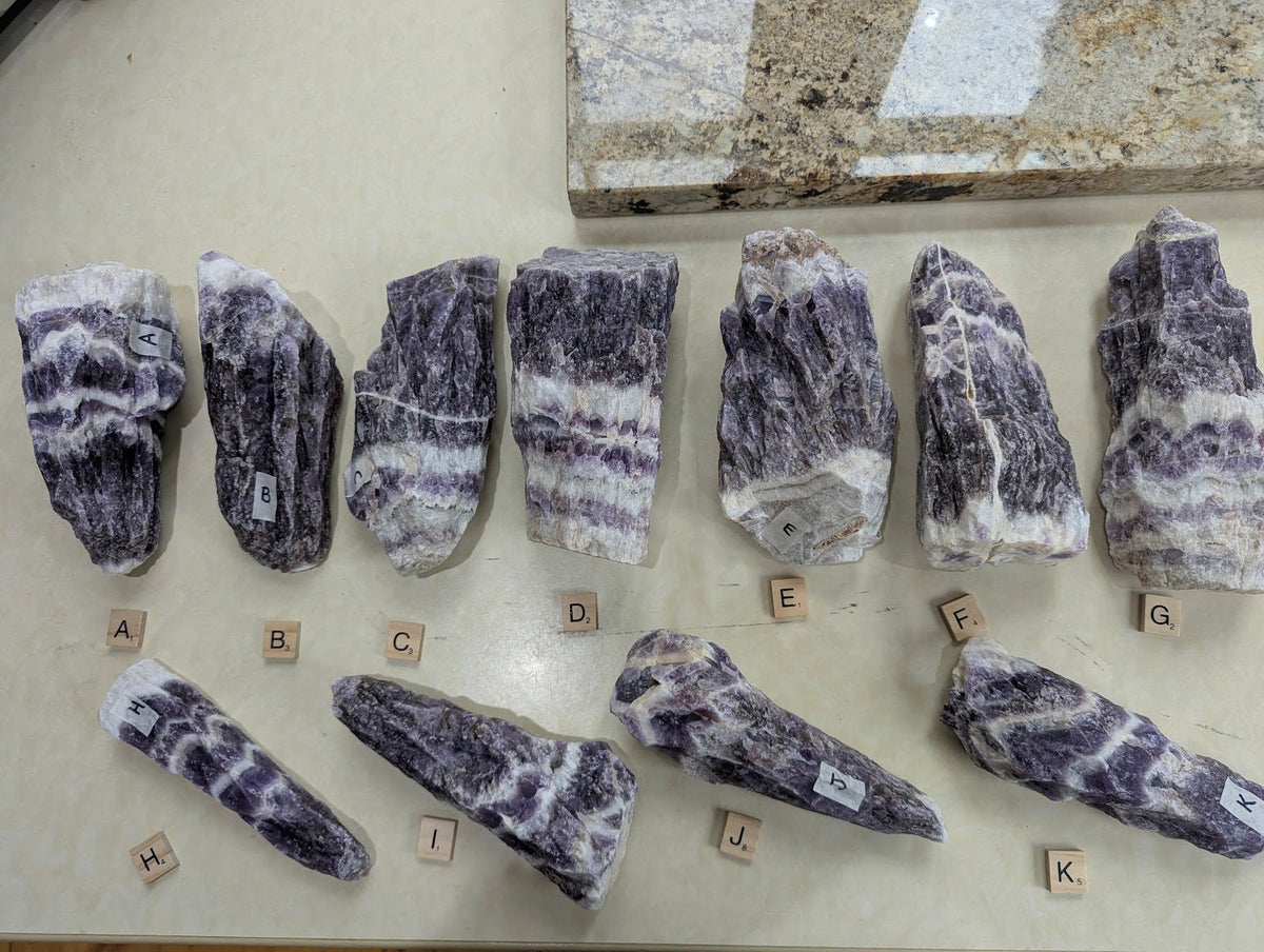 A full collection of raw Dream Amethyst specimens lined up, showing variations in size, texture, and deep purple chevron banding.