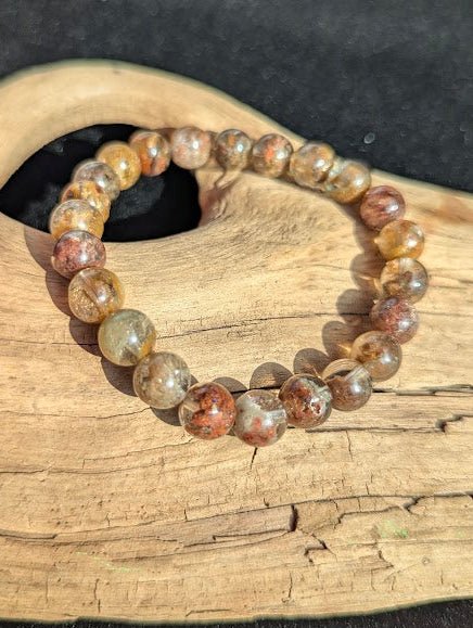 Intuitively selected 8mm AA Grade Four Season Garden Quartz beaded stretch bracelet displayed on driftwood, showing highly transparent quartz with multi-coloured inclusions.