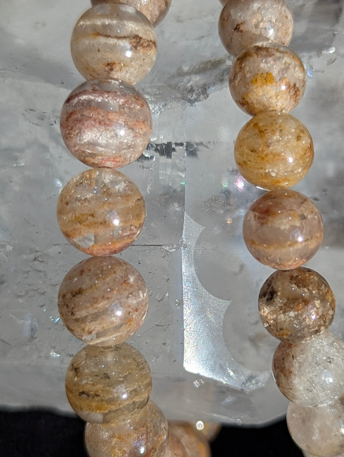 Macro close-up of 8mm Garden Quartz beads resting on a raw clear mineral, highlighting the high transparency and internal earth-toned mineral deposits.
