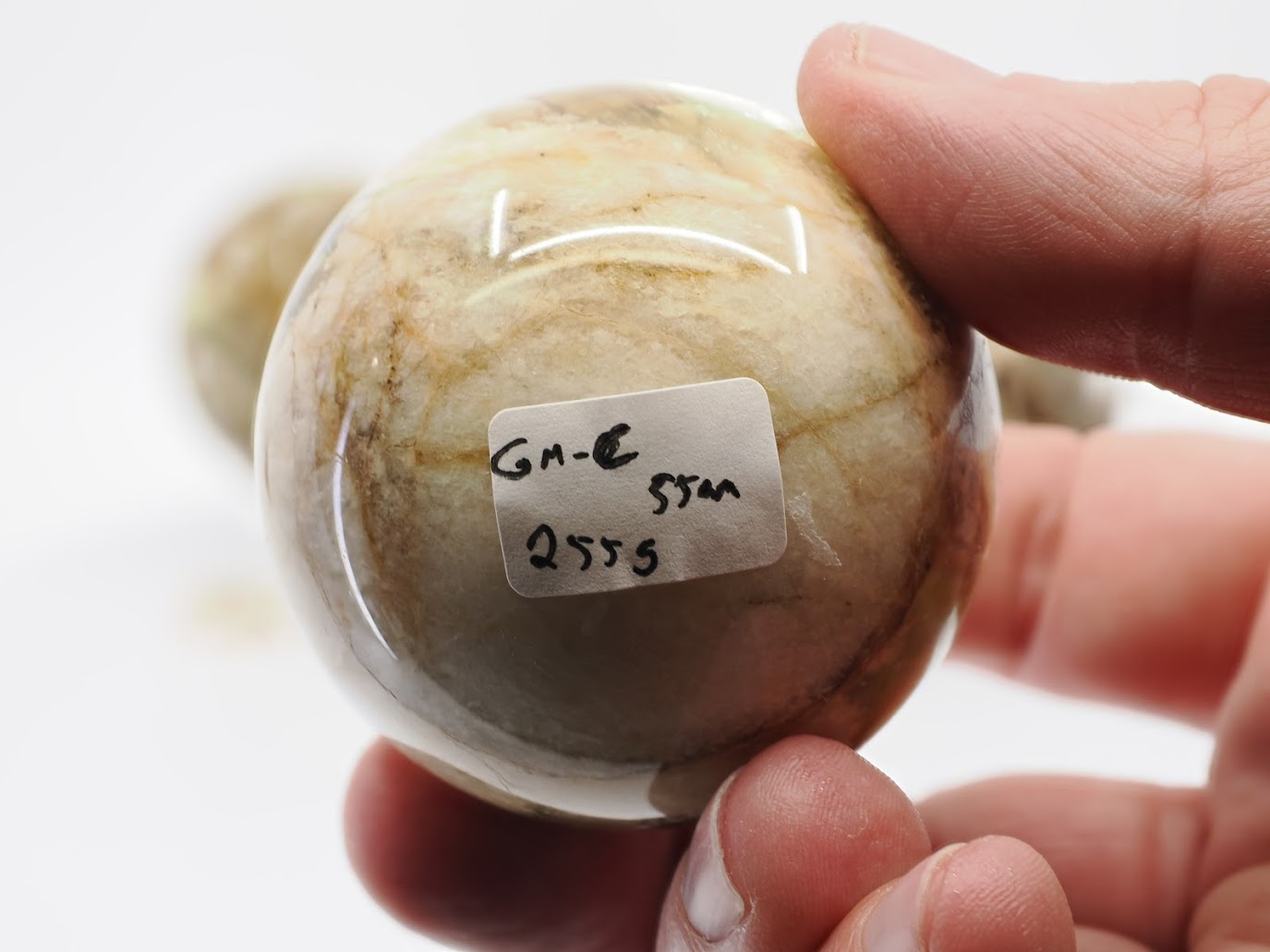 Close-up of Golden Mica sphere C showing 55mm size and 255g weight label against a creamy white and gold mica matrix.