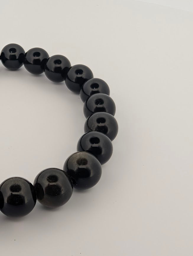 Angled close-up highlighting reflective gold ribbons across obsidian beads