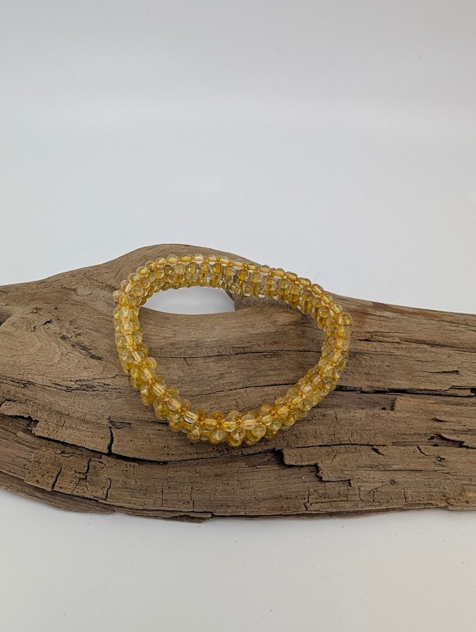 Golden Rutilated Quartz bracelet with golden rutile threads displayed on driftwood