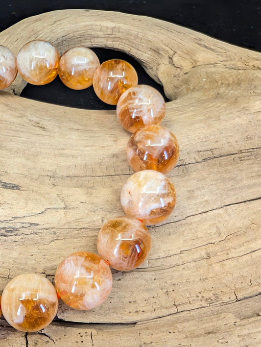 Macro view of Golden Sericite Phantom Quartz beads showing internal silky mica plumes and orange phantom crystal structures.