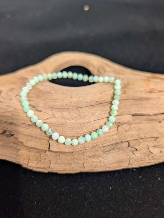 3mm faceted Green Opal beaded stretch bracelet resting on a driftwood display, showing soft mint green colouration.