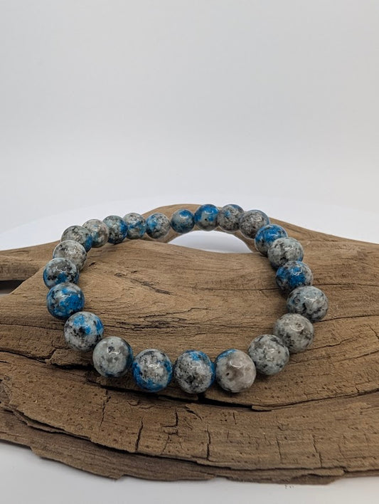 K2 stone 8mm round bead stretch bracelet on driftwood showing grey granite with blue azurite orbs