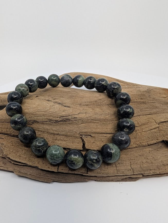 Kambaba Jasper 8mm round bead stretch bracelet on driftwood showing deep green and black orbicular patterns