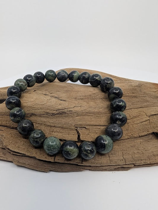 Kambaba Jasper 8mm round bead stretch bracelet on driftwood showing deep green and black orbicular patterns