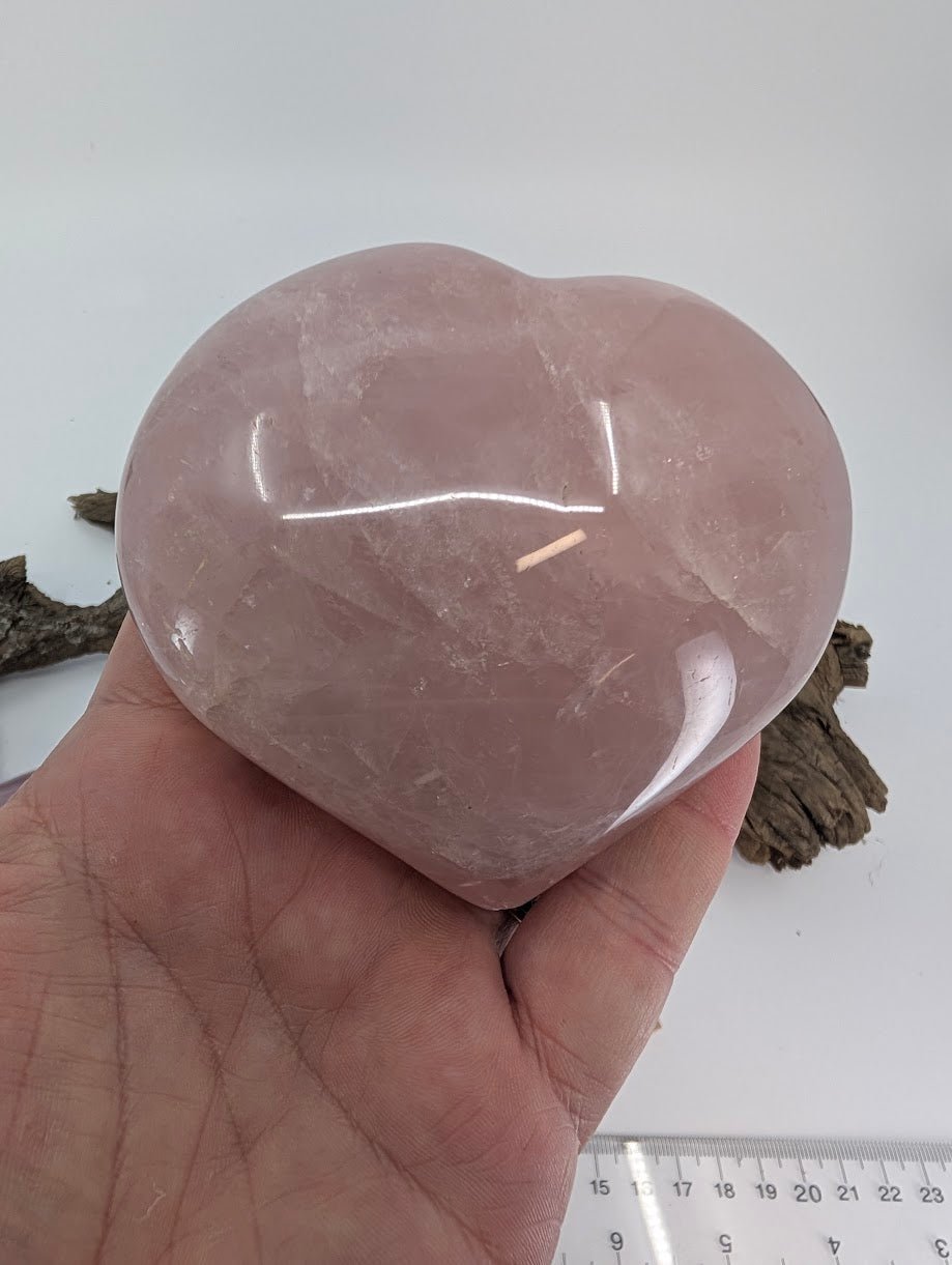 Hand holding Specimen B, a massive 560g Rose Quartz heart, showing thickness and scale.