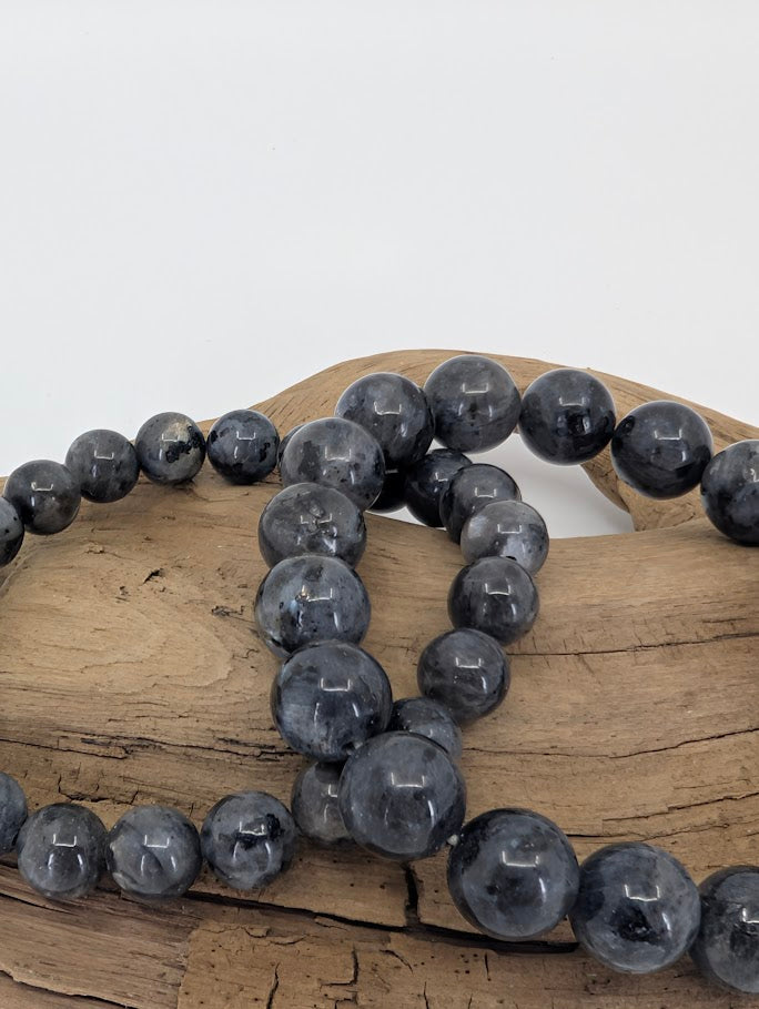 Larvikite bracelet with 8mm and 10mm round beads on driftwood, closeup angle