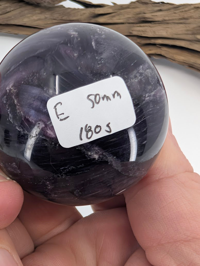 Hand holding 49mm Lepidolite Sphere E with size and weight sticker visible.