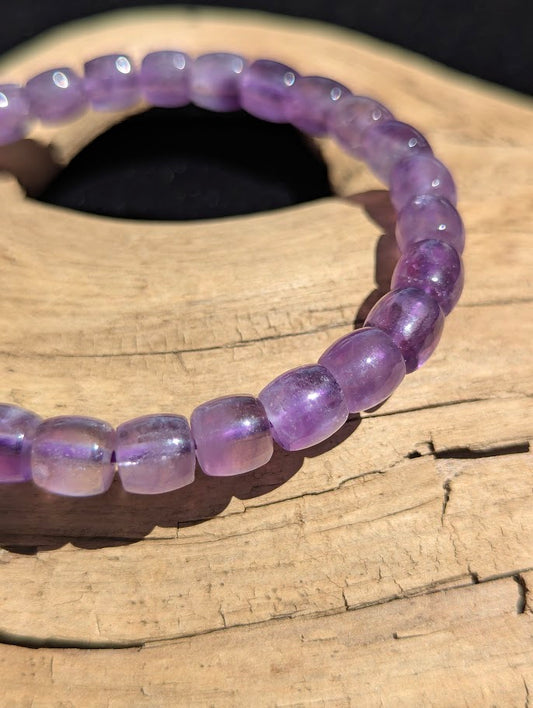 Macro close-up of 7mm polished Amethyst barrel beads highlighting the smooth cut, natural internal veiling, and the purple elastic cord visible through the quartz.