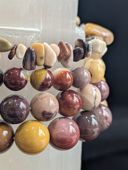 Detailed view of Mookaite lapidary bracelets displayed on a crystalline Selenite tower, highlighting their high vitreous luster and contrasting boundary lines.