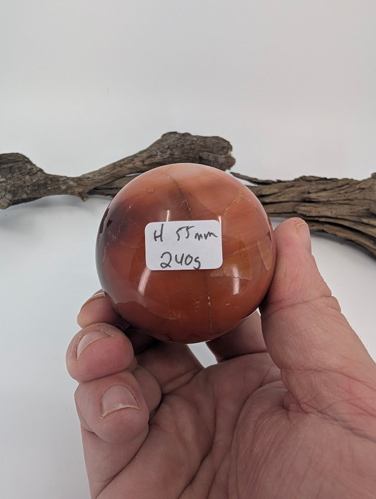 Hand holding Mookaite sphere H with weight label (240g).