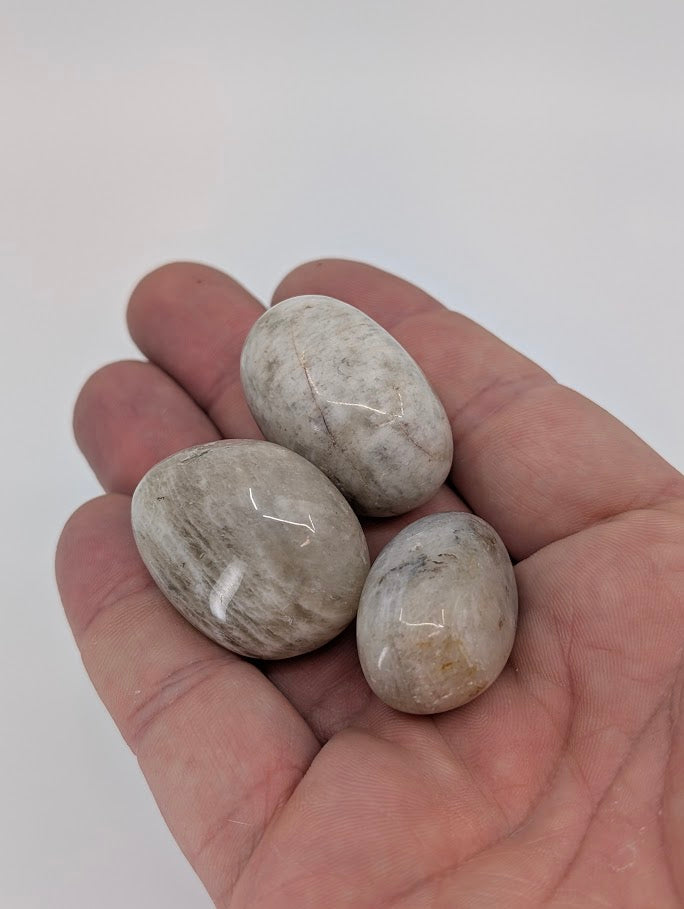 Moonstone tumbled stones in hand for size reference