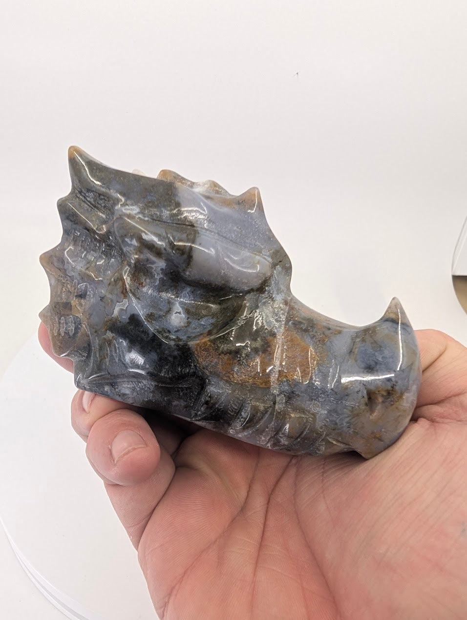 Handheld view showing moss inclusions inside grey chalcedony dragon carving