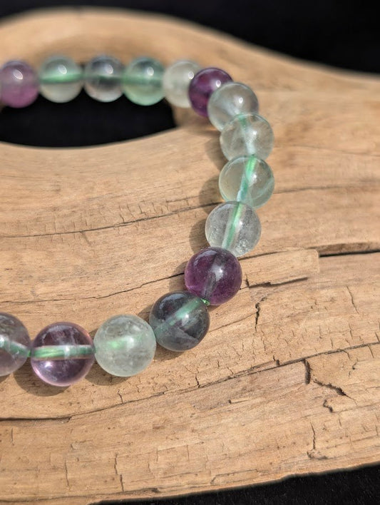 Macro close-up of 8mm translucent green and purple fluorite beads showing natural internal structures and a green stretch cord.