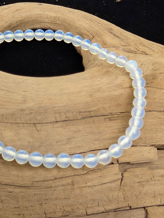 Macro close-up of 4mm polished Opalite beads highlighting the high-gloss finish and the Tyndall effect glow.