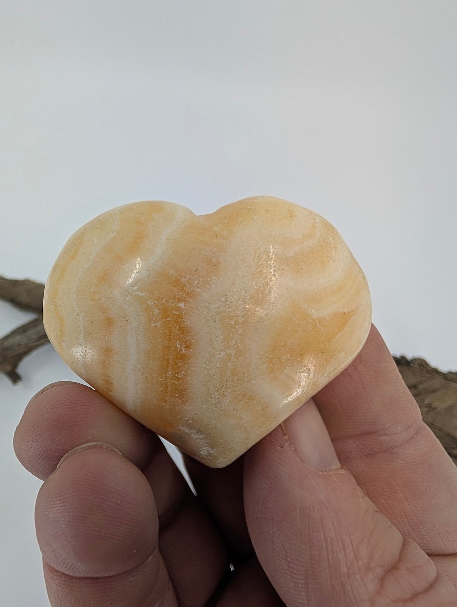 Hand holding a small 60g Orange Calcite heart showing waxy luster.