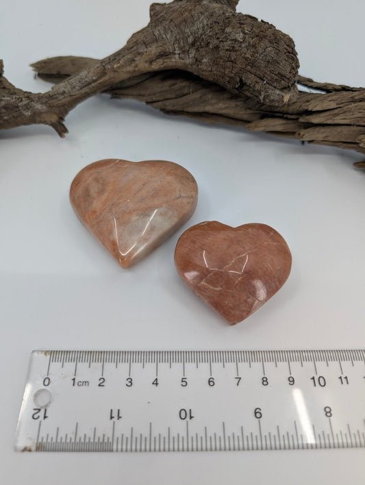 Pair of Peach Moonstone hearts showing warm tan and apricot colors on driftwood.