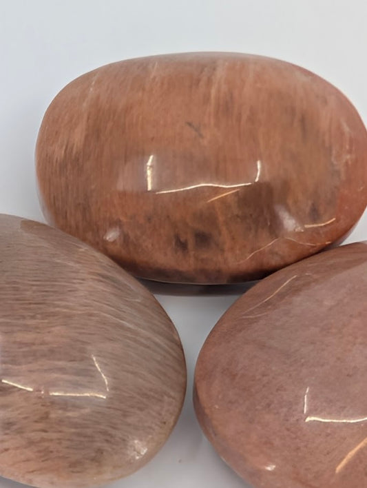 Peach Moonstone palm stones grouped together showing gentle chatoyancy and warm glow