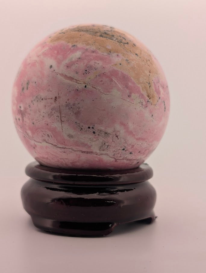 Side profile of Peruvian rhodonite sphere on dark wood stand