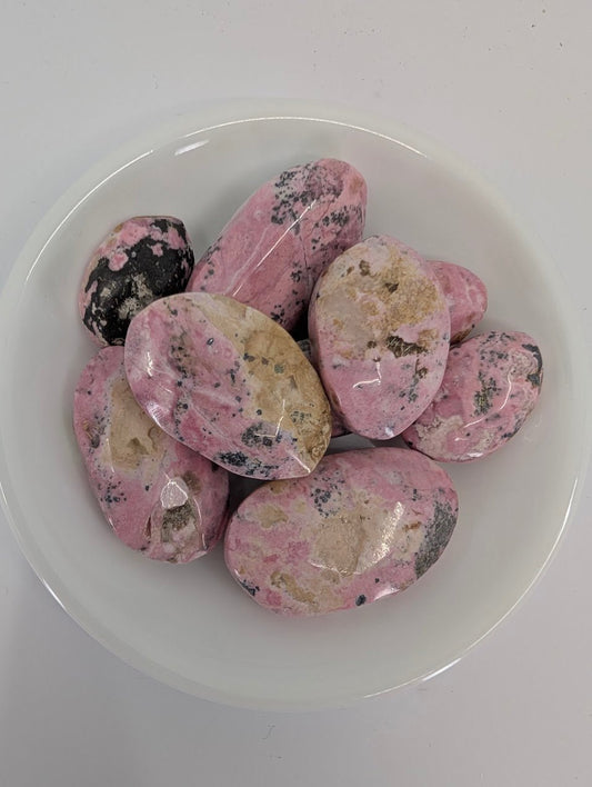Close-up of Pink Rhodonite tumbled stones from Peru showing natural pink tones, beige patches, and charcoal flecks