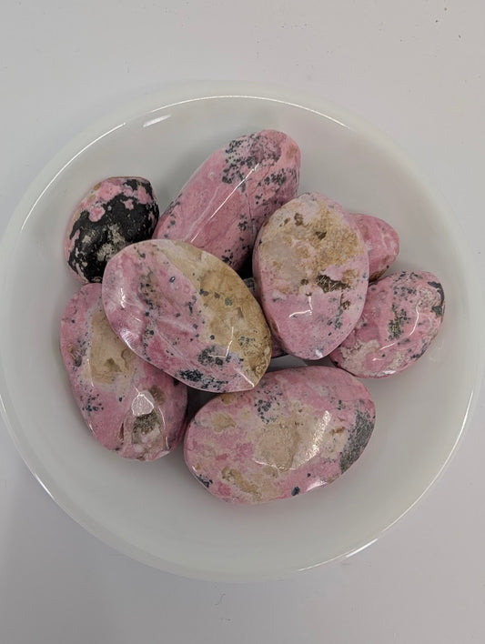 Close-up of Pink Rhodonite tumbled stones from Peru showing natural pink tones, beige patches, and charcoal flecks