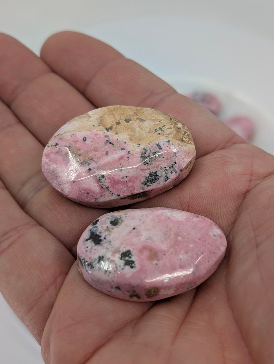 Hand holding Pink Rhodonite tumbled stones from Peru to show size, polish, and thickness