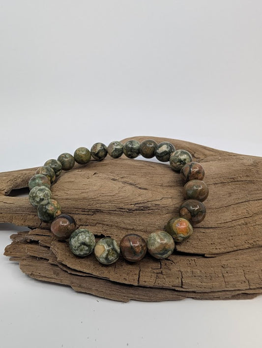 8mm rainforest jasper bracelet with mossy green and brown orbs displayed on driftwood