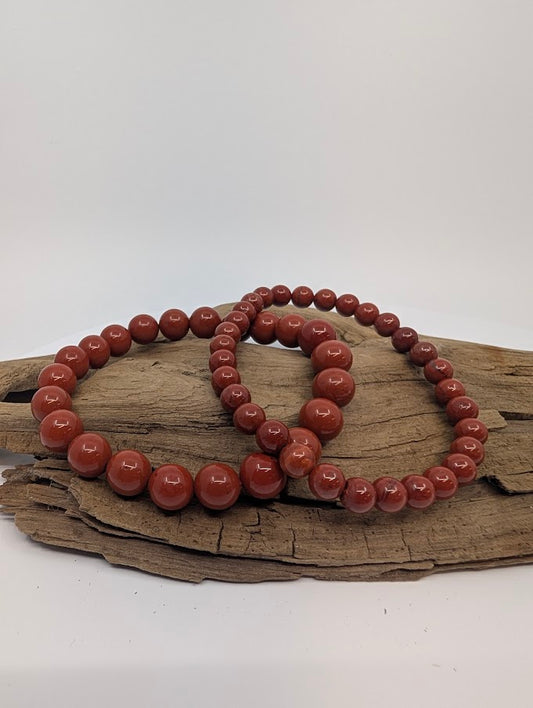 Two red jasper bracelets, 6mm and 8mm, displayed on driftwood