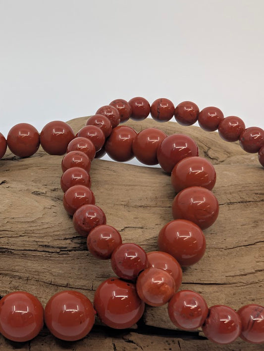 Red jasper bead bracelets set on driftwood, lifestyle image