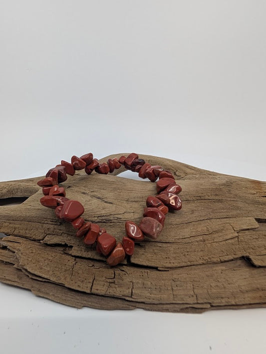 Red jasper chip bracelet with rich brick-red polished stones displayed on driftwood