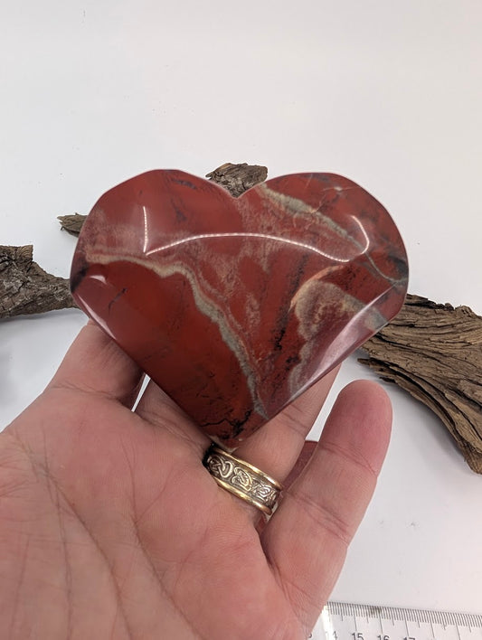 Hand holding a large 210g Red Jasper heart to show substantial palm size and glossy polish.