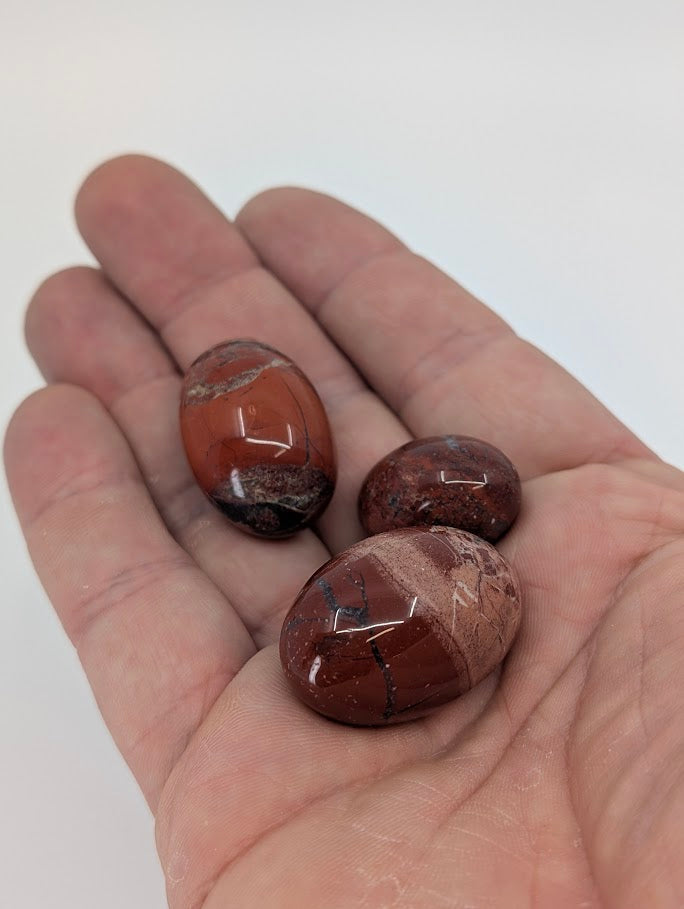 Red Jasper tumbled stones in hand for size reference