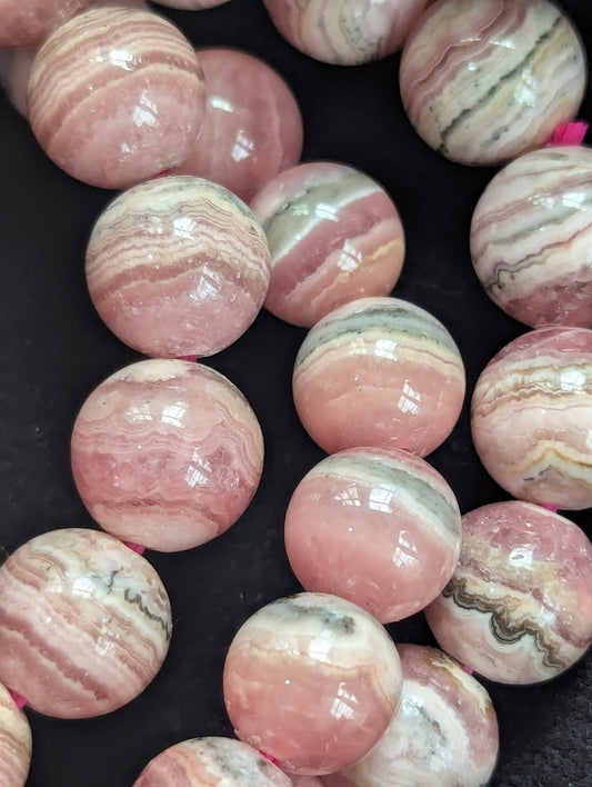 Macro close-up of Argentinian Rhodochrosite beads highlighting distinct stalactitic growth layers and raspberry-pink tones.