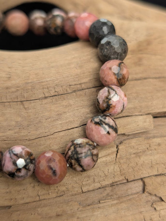 Macro close-up of 8mm faceted Rhodonite beads highlighting geometric surface cuts and black manganese oxide veining.