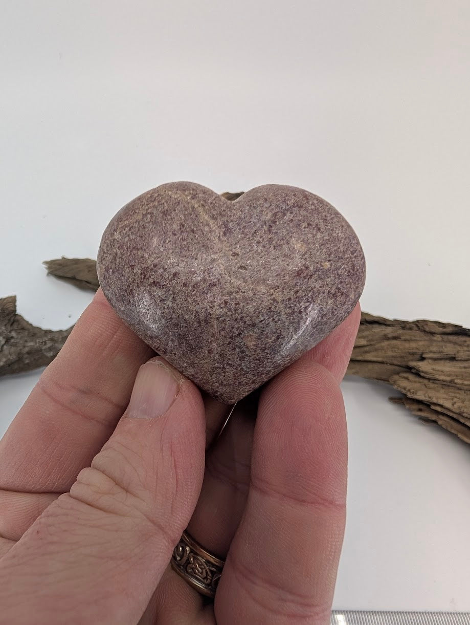 Hand holding a 85g Rhodonite heart to show size and granular texture.